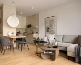 Beżowy salon inspiracje: przytulna przestrzeń z szarą sofą, drewnianym stołem i nowoczesną kuchnią.