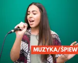 Młoda kobieta z mikrofonem w dłoni, wpatrzona w dal, z otwartymi ustami, jakby wykonywała śpiew operowy.