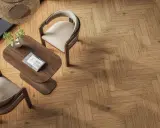 Drewniana podłoga z klasycznym wzorem jodełka, dwa krzesła i stolik kawowy tworzą przytulną przestrzeń.