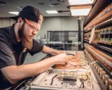Młody technik w okularach ochronnych pracuje przy panelu z przewodami. To przykład praktycznego zastosowania wiedzy z zakresu mechatronika co to jest.