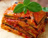 Une part généreuse d'aubergine parmigiana, empilée et nappée de sauce tomate, garnie de feuilles de basilic frais.
