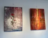 Två abstrakta målningar på väggen. Till vänster en röd blomma på en mörk bakgrund, en fin diy canvas. Till höger en stadssilhuett i varma färger.