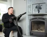 Sotare rengör en braskamin med en dammsugare. Frågar du dig "vad kostar sotning av braskamin"?