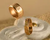 Due anelli d'oro con incisioni uniche, che mostrano diversi tipi di fedi nuziali, su una pietra a forma di mano con sabbia.