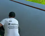 Pracownik w koszulce z napisem "POSADZKI ŻYWICZNE" wykonuje prace na ciemnej powierzchni.