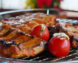 Costillas de cerdo y tomates rellenos en una parrilla. El tiempo que tarda el carbón en hacer brasa es clave para esta deliciosa cocción.