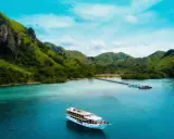 Un'isola lussureggiante con colline verdi e un mare turchese, dove si trova Bali, con una nave da crociera che naviga nelle acque cristalline.