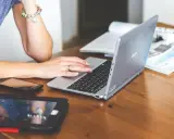 Nauczycielka pracuje na laptopie, który może być zakupiony dzięki bonowi na laptopa dla nauczycieli. Obok leżą tablet i telefon.