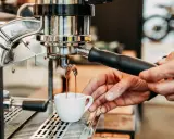 Frisch gebrühter Kaffee fließt aus der Espressomaschine in eine kleine Tasse.