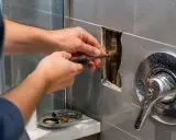 Main tenant utilise un tournevis pour installer une colonne de douche. Les tuyaux en laiton sont visibles dans le mur.