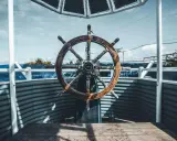 Roue de gouvernail en bois patiné, prête à barrer un bateau vers l'horizon bleu.