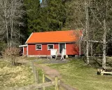Rött torp med orange tak, omgivet av skog. En stig leder fram till torpet Freden, där picknickbord står redo för besökare.