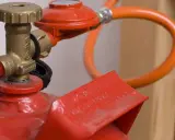 Détail d'une bouteille de propane rouge avec détendeur et tuyau orange, illustrant la norme d'installation gaz propane bouteille.
