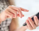Dłoń trzymająca smartfon, palec wskazujący dotyka ekranu.