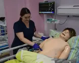 Studentka stomatologii ćwiczy procedury medyczne na fantomie. Monitor parametrów życiowych pokazuje dane.