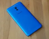 Niebieski smartfon Meizu M6 Note z podwójnym aparatem z tyłu leży na drewnianym blacie.