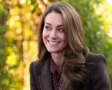 Kate Middleton sonríe con calidez, con su cabello castaño cayendo en cascada. El fondo bokeh de tonos otoñales complementa su elegante atuendo.