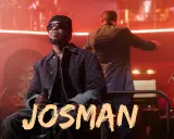 Josman, francuski rap artysta, siedzi na scenie z mikrofonem, w tle orkiestra i dyrygent.