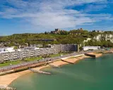 Vista aerea del porto di Dover con il castello in cima alla scogliera bianca. Edifici moderni e spiagge sabbiose si affacciano sul mare turchese.