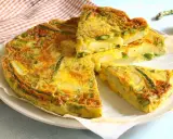 Una gustosa frittata di asparagi, con patate e uova dorate, tagliata a fette su un piatto bianco.