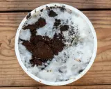 Culture de champignon sur marc de café dans un récipient blanc, sur fond de bois. Le mycélium blanc envahit le marc brun.