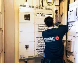 En elektriker arbetar vid en elcentral med många säkringar och mätare. För säkerheten måste man ha jordfelsbrytare.