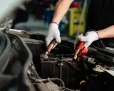 Manos enguantadas conectando cables a la batería del coche. Es hora de desconectar la batería del coche para un mantenimiento seguro.
