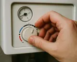 Dłoń reguluje pokrętło pieca gazowego, ustawiając optymalną temperaturę.