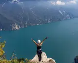 Kobieta z rękami w górze na szczycie klifu, podziwiająca jezioro Garda po przejściu via ferrata.