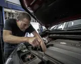 Mechanik w okularach ochronnych pracuje przy silniku samochodu. Zastanawiasz się, ile kosztuje wymiana oleju?