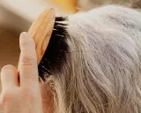 Une main brosse des cheveux gris, secs, peut-être liés à la ménopause, avec une brosse en bois.
