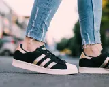 Nogawki jeansów i czarne **modele butów adidas z lat 2000.** ze złotymi paskami i różową podeszwą.