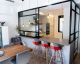 Tabique cocina semiabierta al salón con barra y taburetes coloridos. La cocina moderna se integra al salón a través de un panel de cristal y metal.