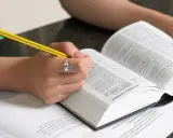 Mani che studiano un dizionario, scrivendo con una matita. Scoprire parole italiane affascinanti è un viaggio.