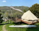 Malowniczy glamping w Polsce z namiotem typu dzwon, tarasem i kajakiem na tle zielonych wzgórz i jeziora.