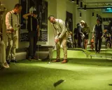 Människor i festliga kläder spelar minigolf på Golfbaren Stockholm.