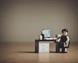 Figurka Lego przedstawiająca zestresowanego pracownika siedzącego przy biurku z komputerem.