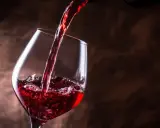 Vino tinto se vierte en una copa, creando burbujas y espuma. Un brindis por el día del vino.