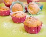 Leckere Muffins ohne Ei, bestäubt mit Puderzucker, in bunten Papierförmchen auf hellgrüner Unterlage.
