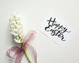 Un giacinto bianco legato con un nastro rosa, accanto a un biglietto con scritto "Happy Easter". Come una poesia campane di Pasqua di Gianni Rodari.