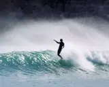 Surfer in Aktion auf einer Welle an der Algarve. Die Gischt spritzt, während er die portugiesische Küste genießt.