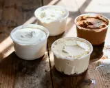 Composition de quatre pots de produits laitiers crémeux, dont une ricotta au chocolat, sur une table en bois rustique.