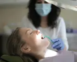 Pacjentka u dentysty, która ma w ustach zieloną końcówkę ssaka stomatologicznego.