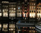 Edifici illuminati e riflessi sull'acqua, un battello turistico naviga tranquillo. Magica atmosfera di Amsterdam by night.
