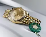Złoty zegarek Rolex, jak brat szpaka, lśni na jasnym tle. Zielona pieczęć "Superlative Certified" podkreśla jego prestiż.
