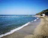 La **spiaggia** di **Castel di Mezzo** baciata dal sole, con il mare azzurro e la collina verde sullo sfondo.