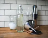 Zutaten für zuckersirup selber machen: Zucker in einem Glas, Sirup in einer Flasche, Cocktail-Shaker und Trichter.