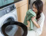 Frau riecht an grüner Kleidung, die sie aus der Waschmaschine nimmt. Sie versucht, den unangenehmen Geruch aus der Kleidung zu entfernen.