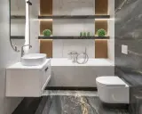 Nowoczesna, mała łazienka z wanną, umywalką nablatową i podwieszaną toaletą. Marmurowe płytki i drewniane akcenty tworzą elegancką przestrzeń.