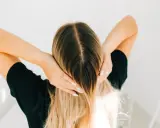 Kobieta z blond włosami, która delikatnie dotyka swojej głowy, jakby stosowała krople żołądkowe na włosy dla ich wzmocnienia.